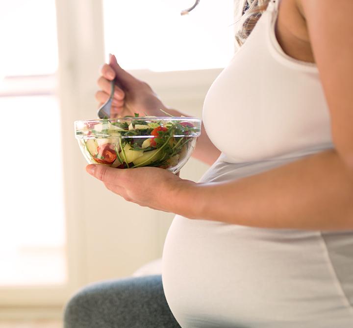 Pregnant woman on healthy diet holding salad